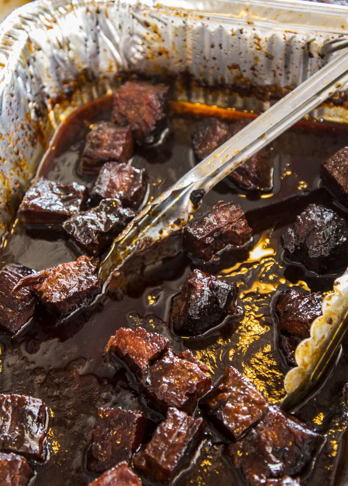 Sauced smoked brisket burnt ends in an aluminum pan.