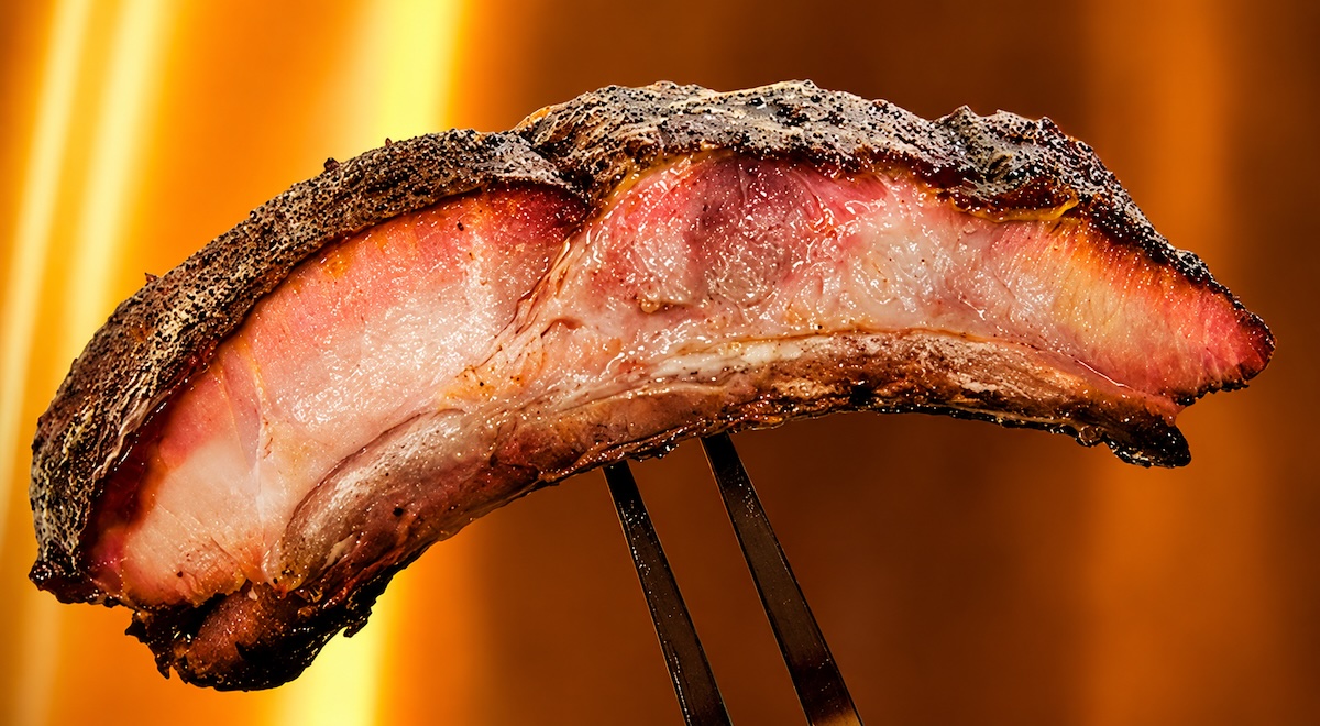 last meal ribs, the best barbecue ribs recipe, shown as a sliced rib on a fork with flames in the background.