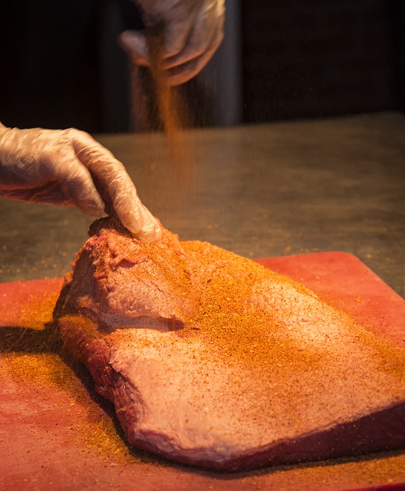 BBQ rub being sprinkled on to brisket.