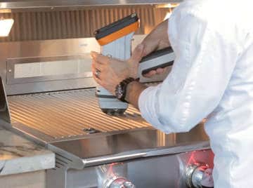 Metalurgy gun. Manin white jacket holds a large plastic tool over a shiny, stainless steel surface.
