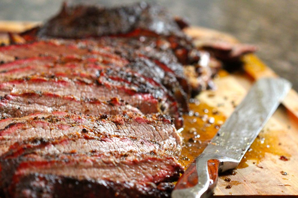 sliced meat from smoked brisket recipe on a cutting board with a knife.