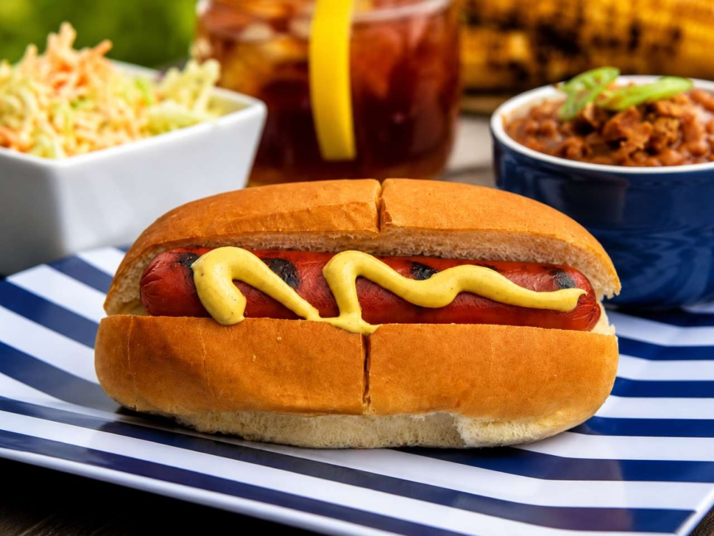 Hot dog on a stripped plate and beans and coleslaw.